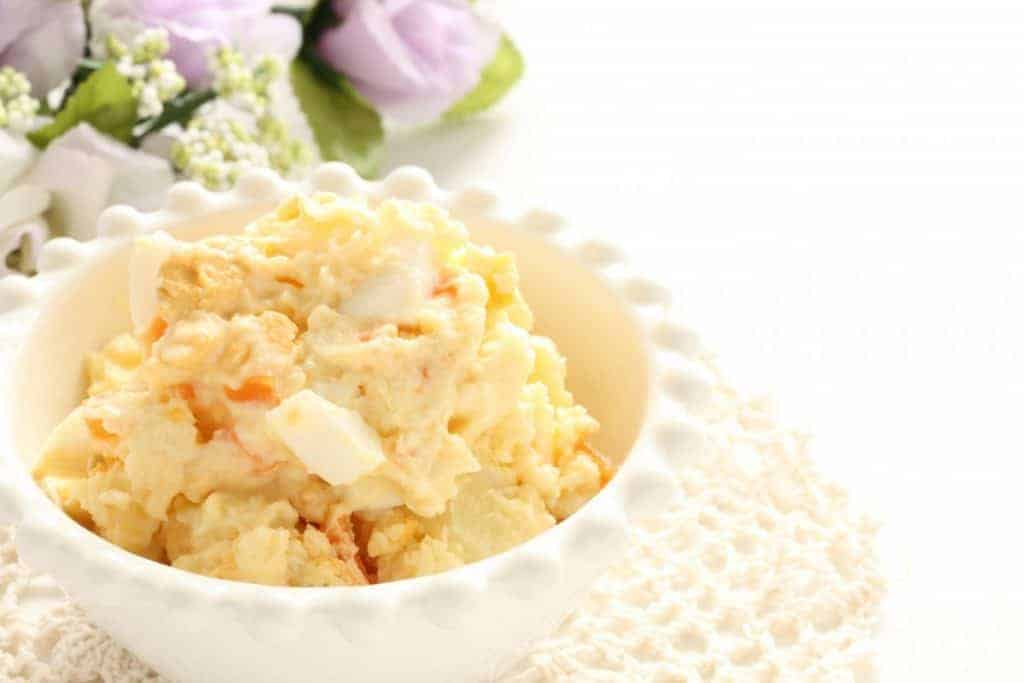 Yellow potato salad in a white bowl.