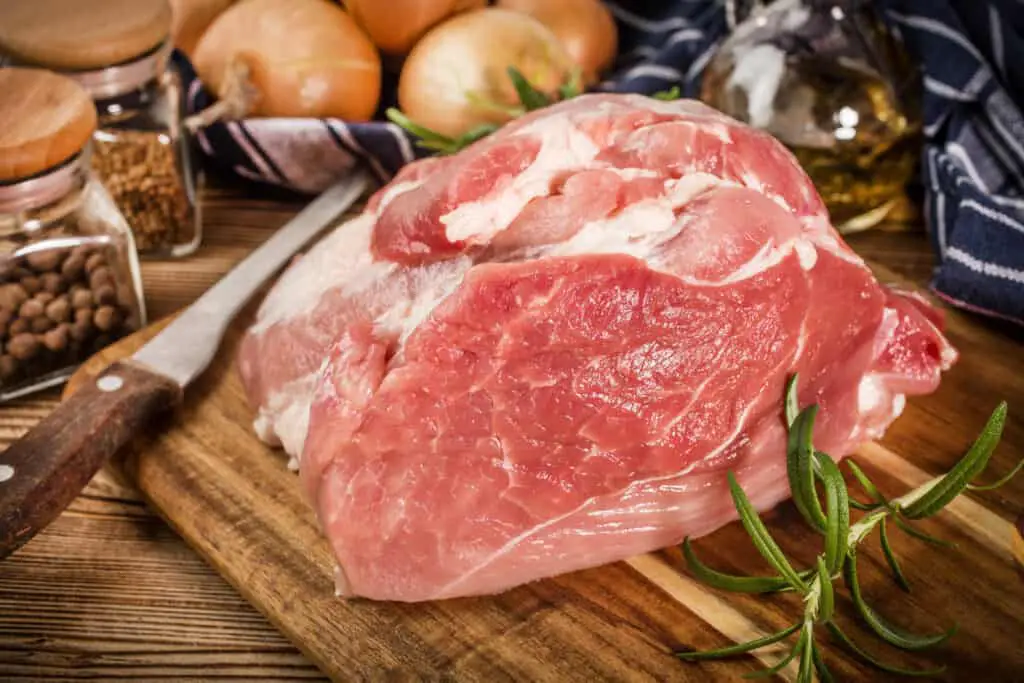 Raw pork shoulder on cutting board with knife.