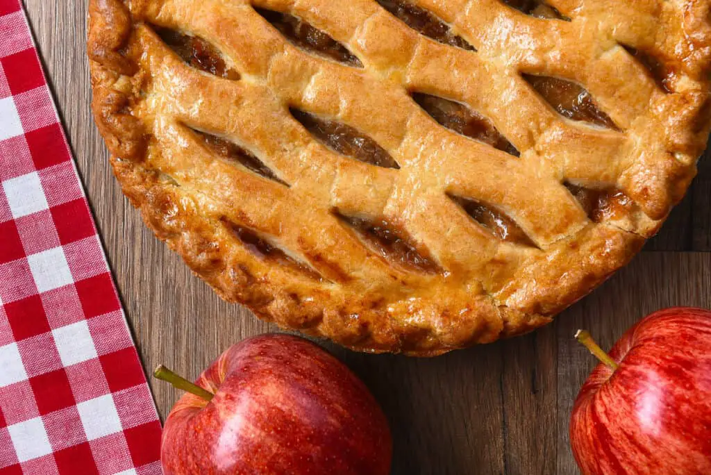 Flat Lay view of a fresh baked apple pie with apples on a rustic wood table.