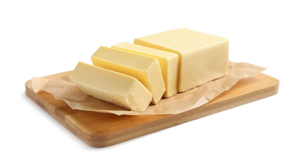 Wooden board with a cut block of butter on white background.