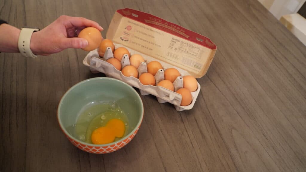 About to crack an egg into a teal and orange bowl.