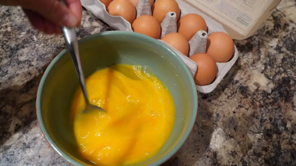Scrambling eggs in a teal bowl.