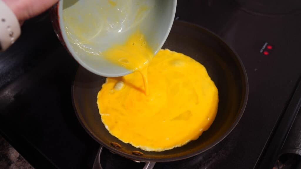 Scrambled eggs being poured into pan on stove.