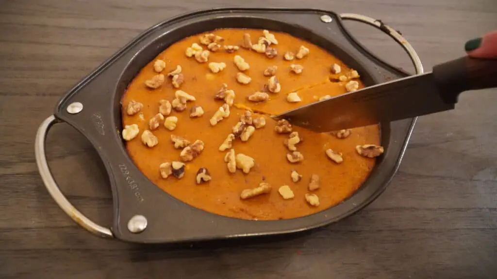 A piece of homemade Pumpkin pie with Walnuts on top is cut from a pan.