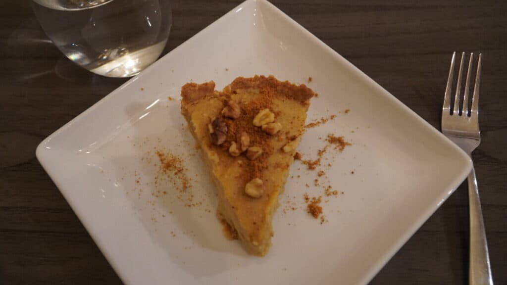 A piece of homemade Sweet potato pie with walnuts and Coconut sugar sprinkled on top on a square white plate.