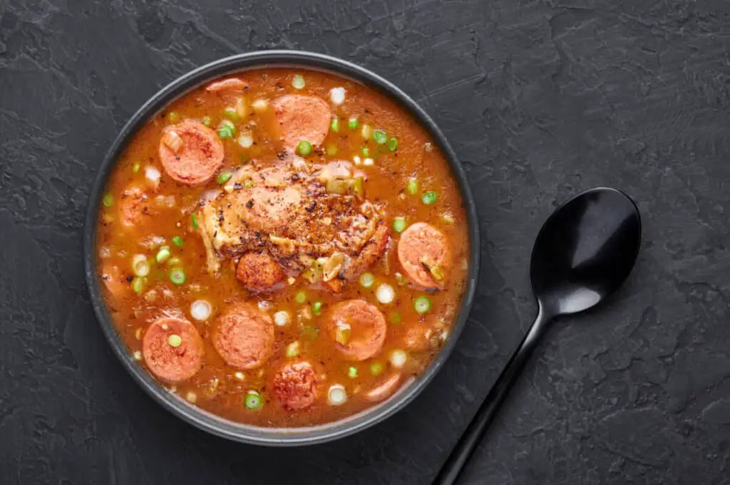 Chicken and Sausage Gumbo soup in black bowl on a dark slate backdrop. Gumbo is Louisiana cajun cuisine soup with a roux. 