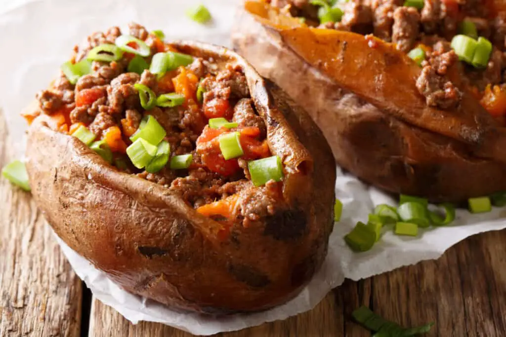 Healthy and tasty food baked sweet potato stuffed with ground beef and green onion close-up on paper on the table.