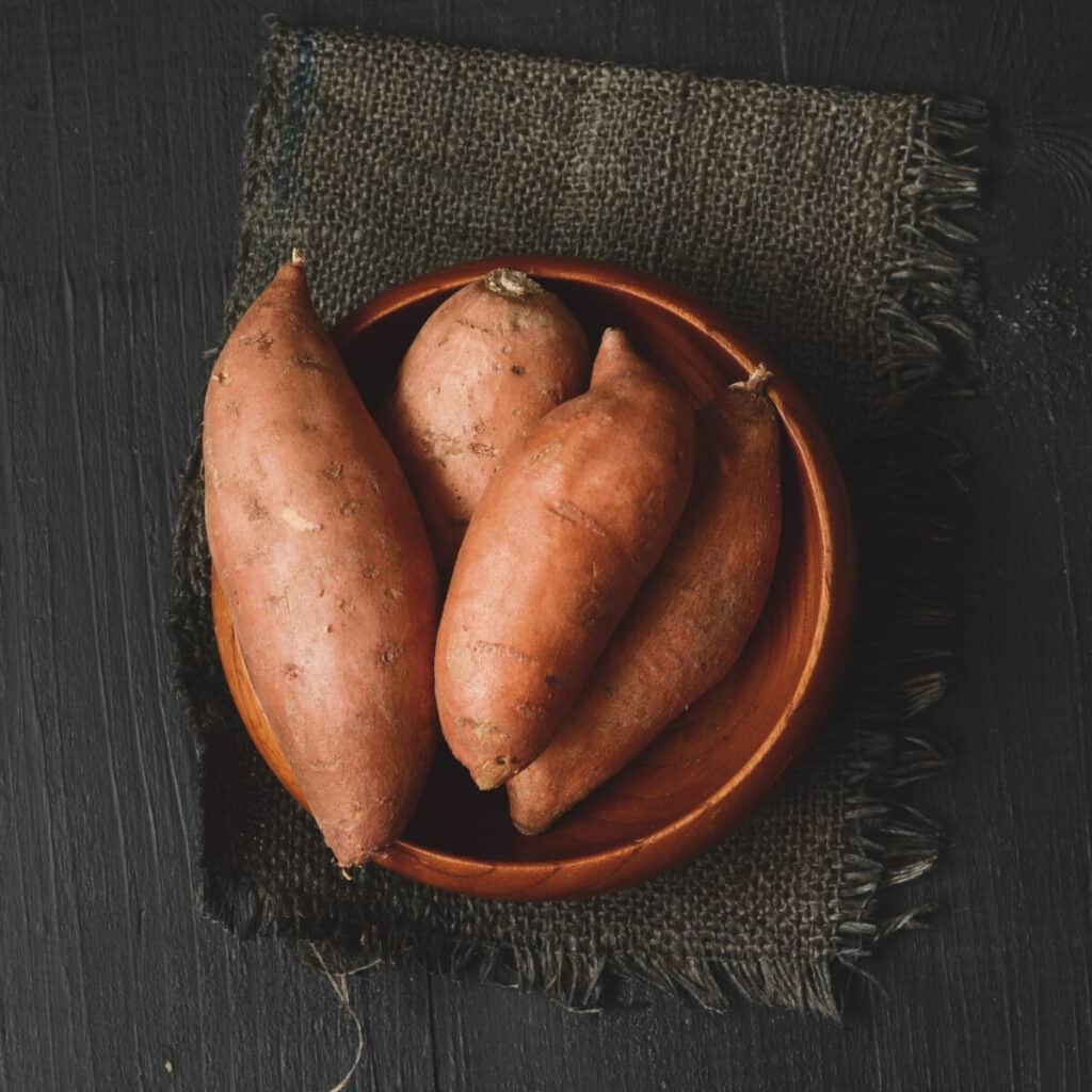 Raw sweet potatoes on dark wooden background.