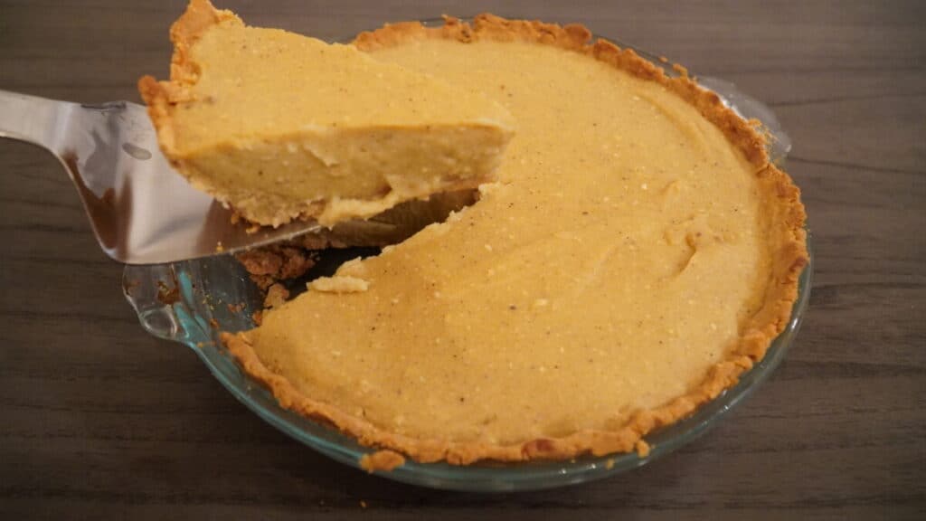 A piece being cut from a Sweet potato pie in a glass dish.