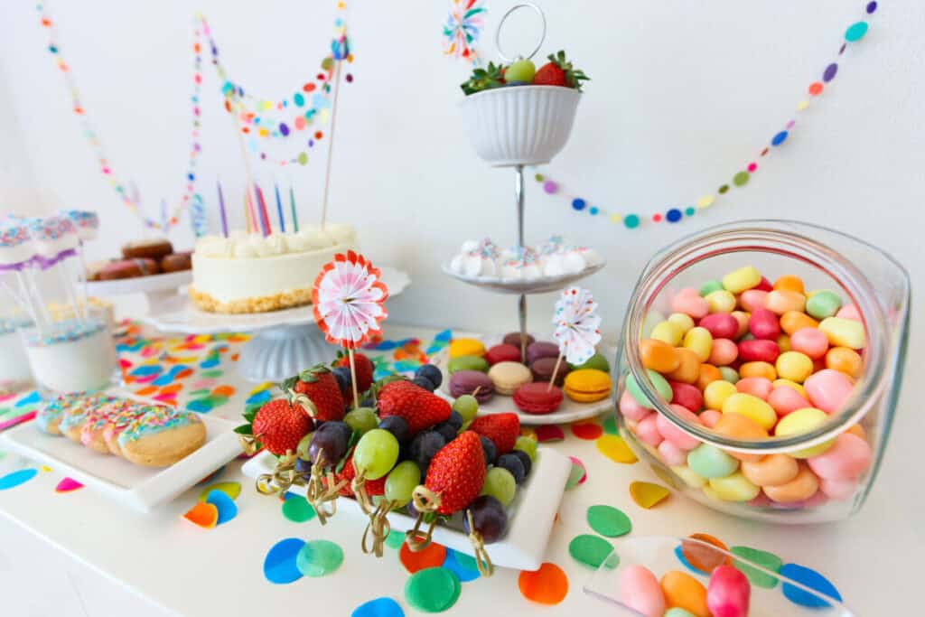 Cake, candies, marshmallows, cake pops, fruits, and other sweets on a dessert table at a kids birthday party