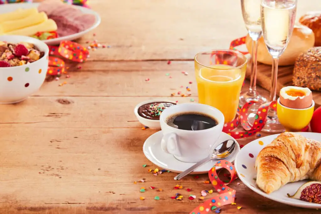 Coffee in a white cup with saucer with festive breakfast or dinner on rustic wooden table border.