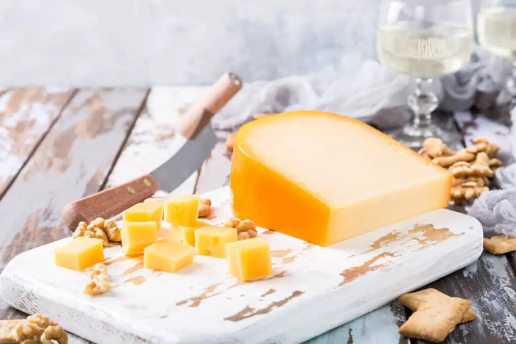 Delicious dutch gouda cheese with cheese blocks, crackers, walnuts, and special knife on a wooden table