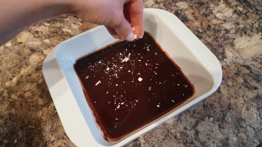 Crushed candy canes being sprinkled on chocolate to make chocolate bark