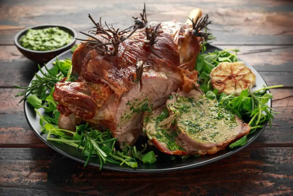 Lamb leg roast with rosemary, herbs, and mint on a black plate