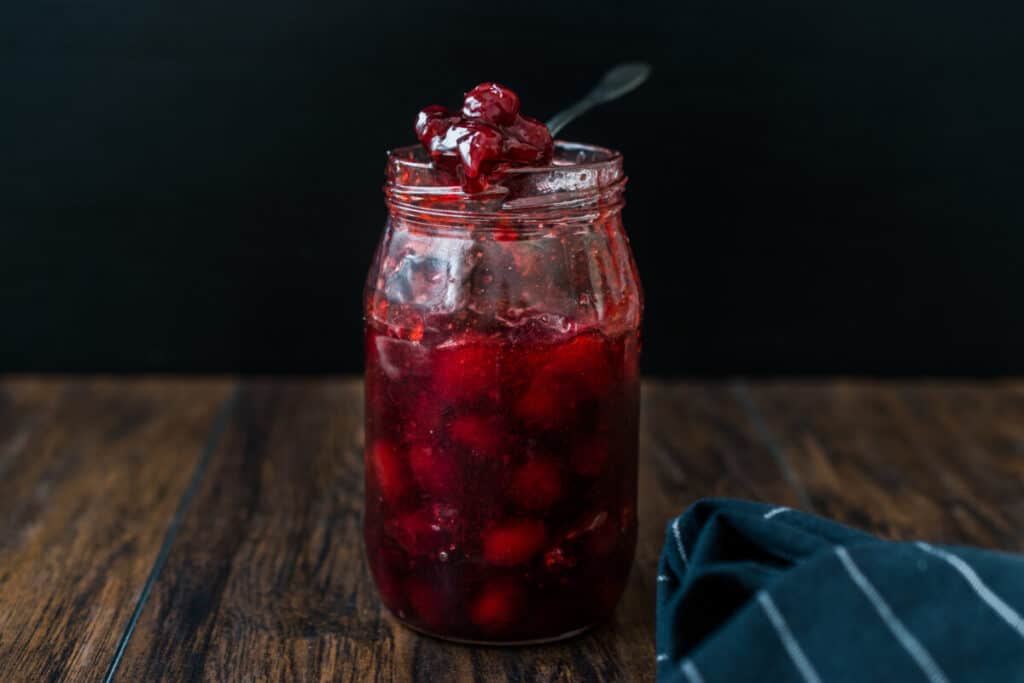 Mason jar with cranberry jam on wooden background