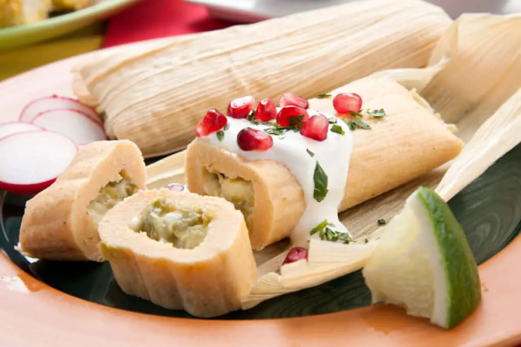 Mexican tamale with marinated corn on a plate garnished with lime and pomegranate seeds.