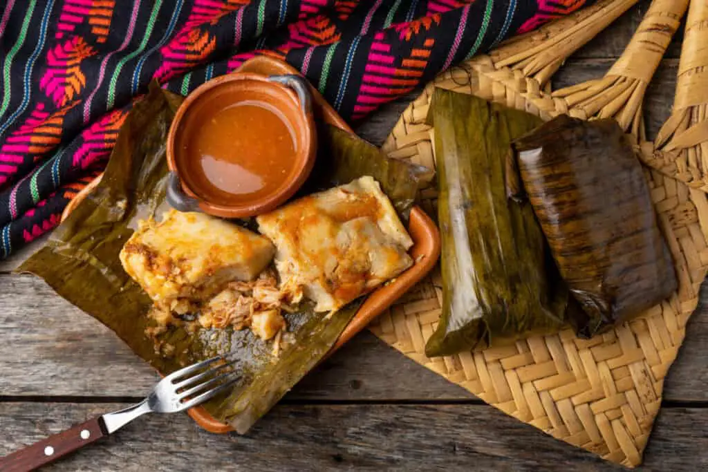 Traditional Mexican tamales wrapped in banana leaves also called "oaxaqueños" on wooden background