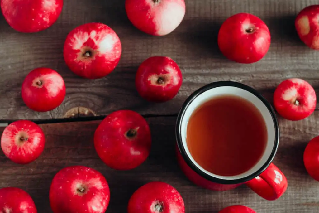 Apple cider in a red cup and ripe red apples on a wooden background
