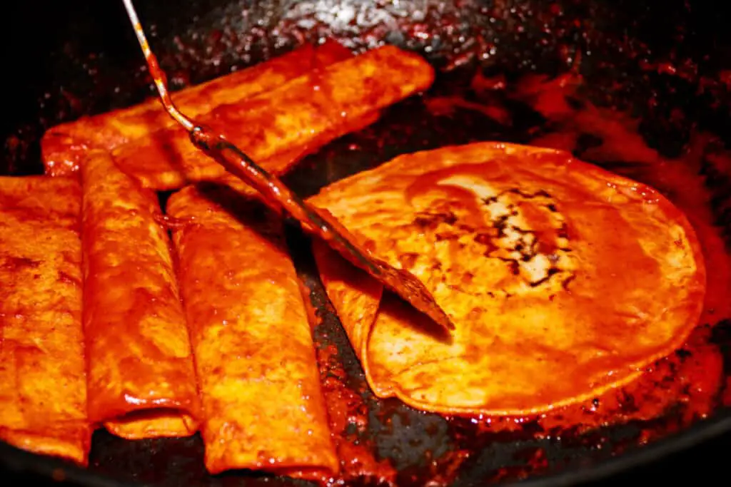 Traditional Mexican enchiladas with red sauce being fried in a pan