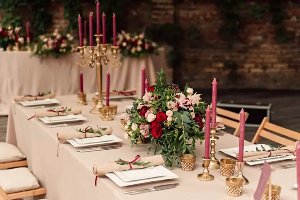 Festive wedding table setting with flowers, napkins, vintage cutlery, glasses, bright table decor details, and candles in a candlestick