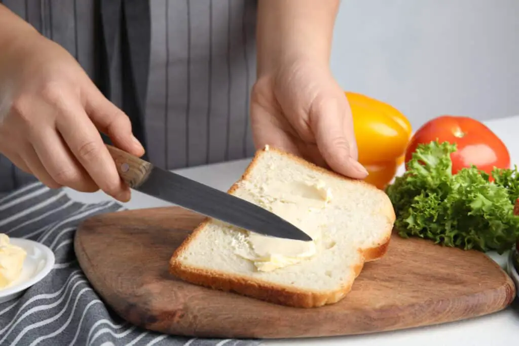 Person spreading butter on white bread