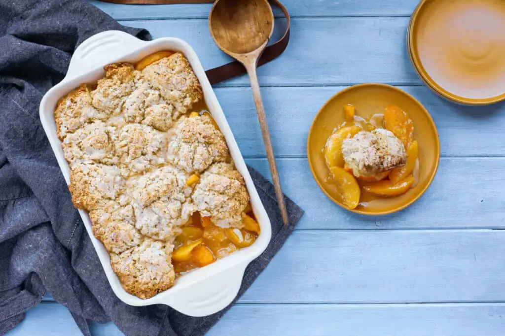 Freshly baked biscuit peach cobbler with apron and wooden spoon shot from top view