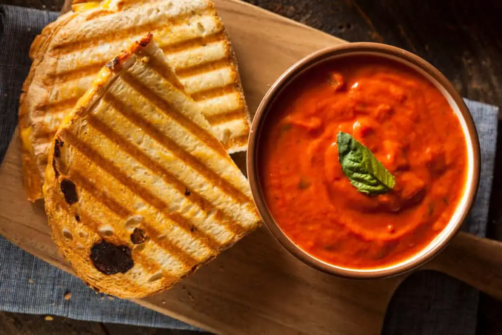 Grilled cheese sandwich and tomato soup on wooden cutting board