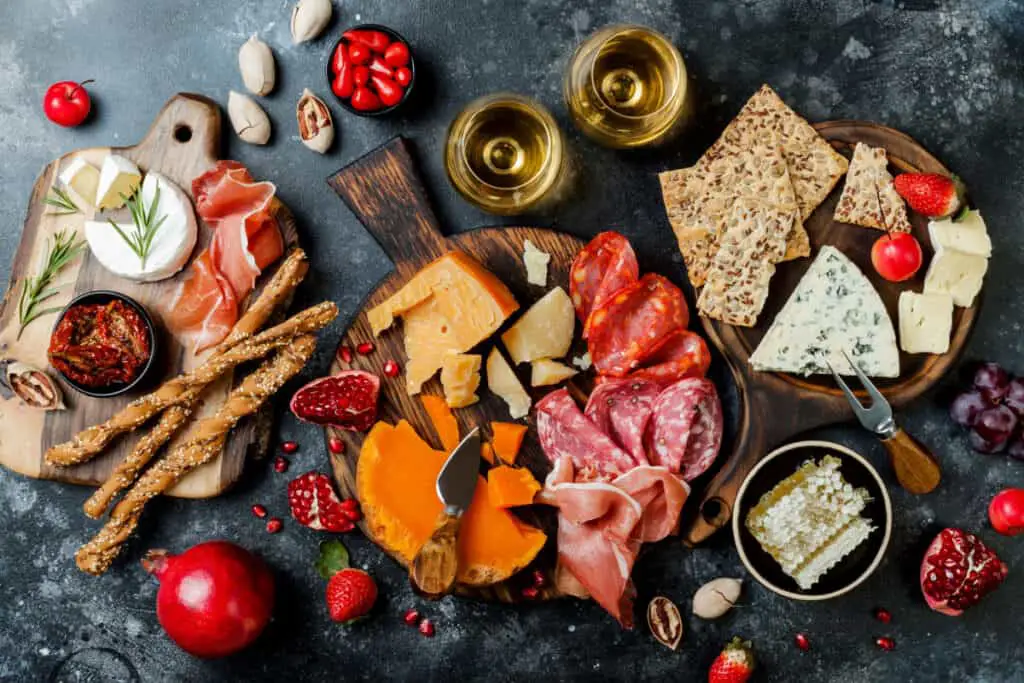 Appetizers table with assorted cheeses, meats, and wine in glasses