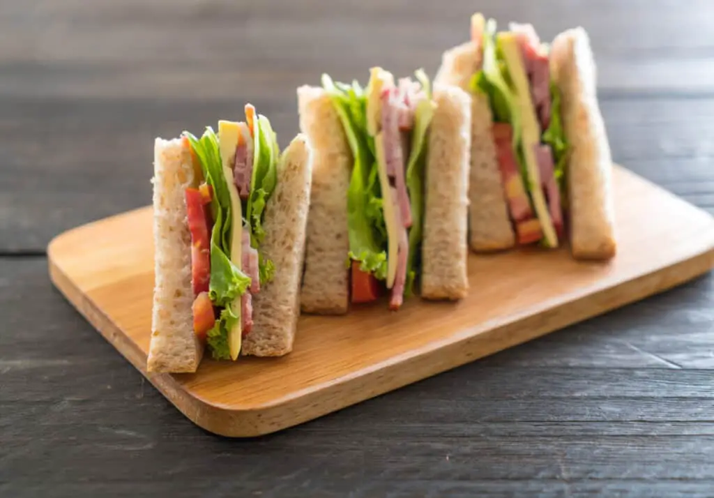 Sandwiches with ham, cheese, lettuce, and tomato on wooden board