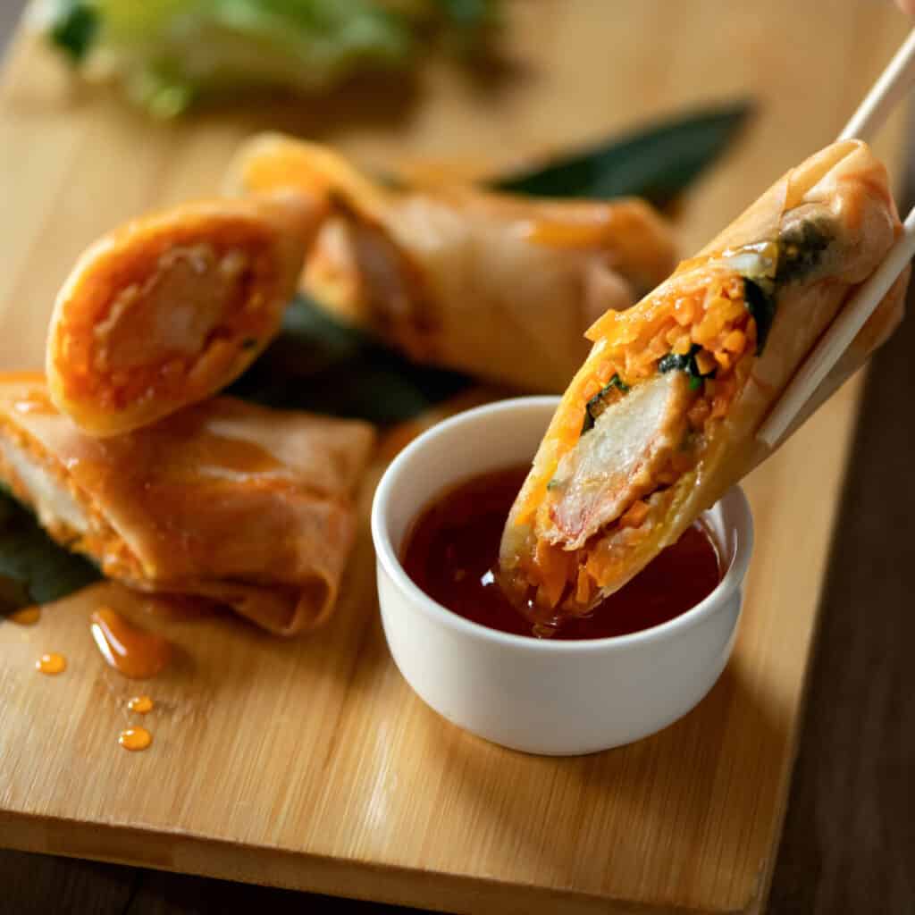 A spring roll being dipped into sweet and sour sauce