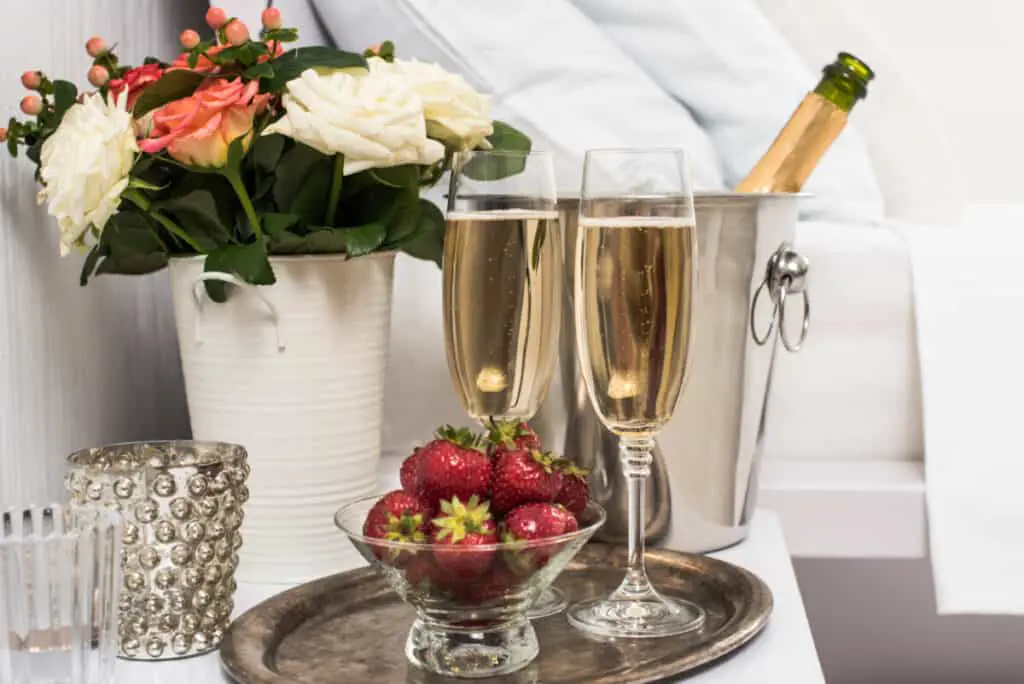 Champagne in a hotel room, ice bucket, glasses and fruits on white linen