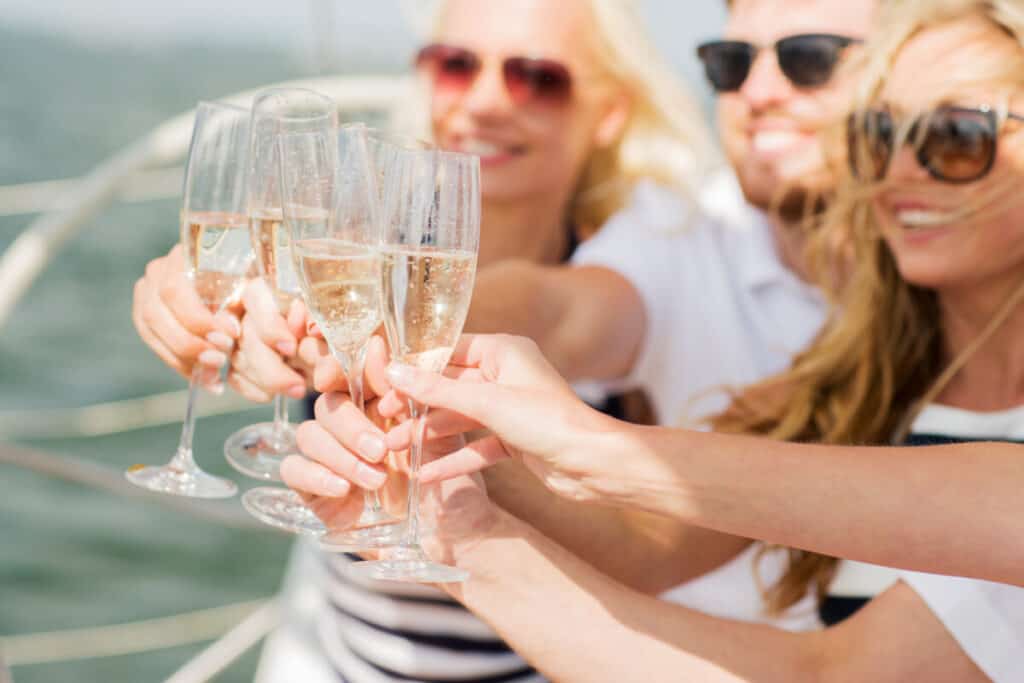 Close up of happy friends clinking glasses of champagne and sailing on yacht