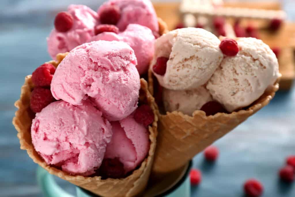 Closeup of creamy raspberry ice cream in waffle cone on a blurred green natural background