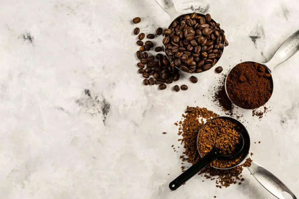 Coffee beans and coffee grounds in measuring cups on granite counter
