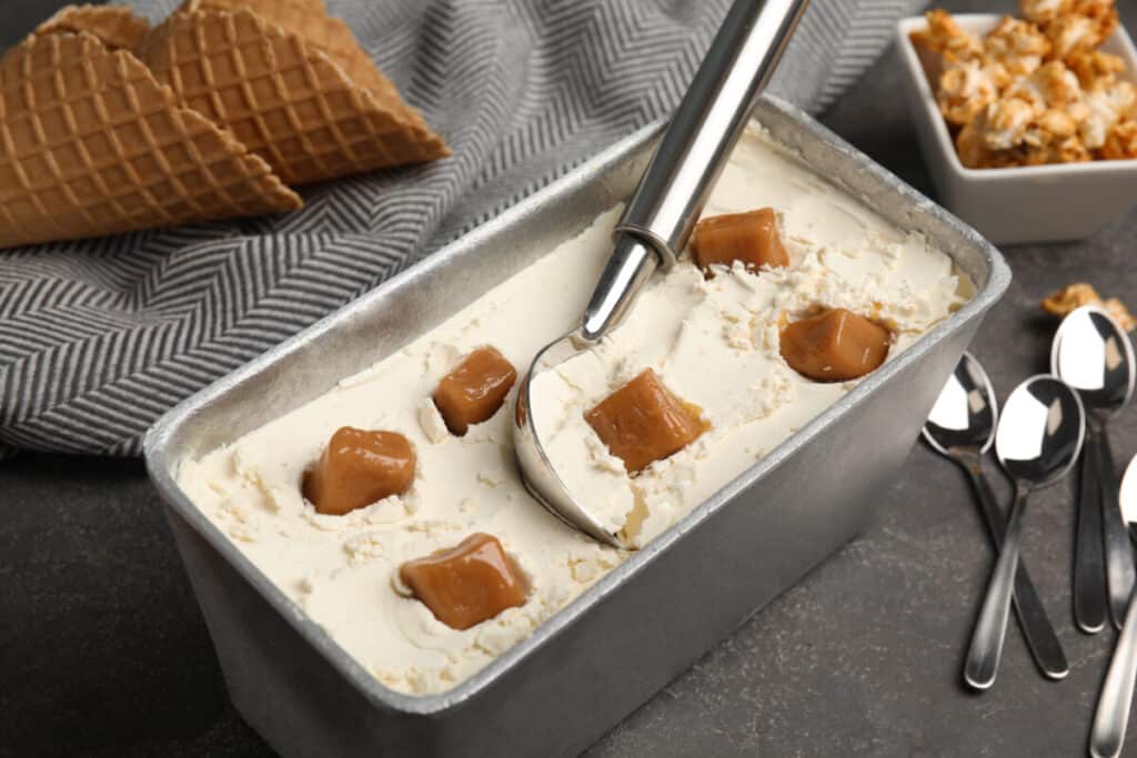 Delicious ice cream in a container with caramel on a table