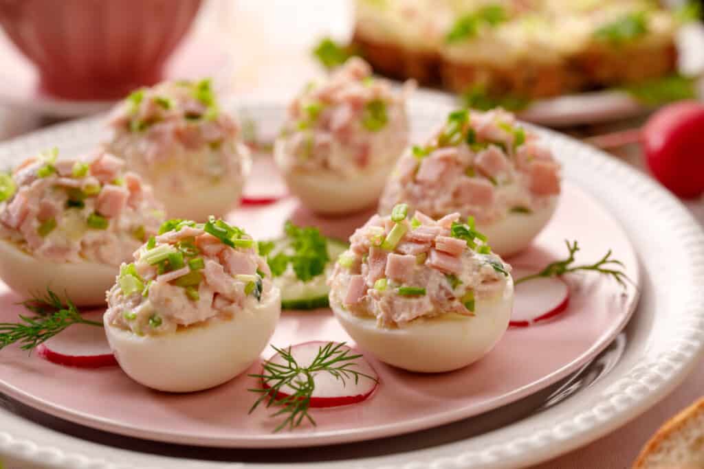 Deviled eggs with ham, chives, radish, and cucumber on a white plate