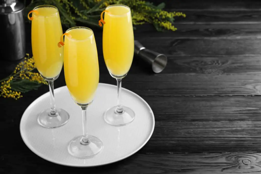 Glasses with mimosa cocktails garnished with lemons on a white plate