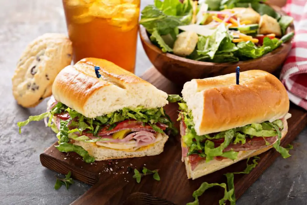 Italian sub sandwich with salami and ham, caesar salad, tea, and cookies