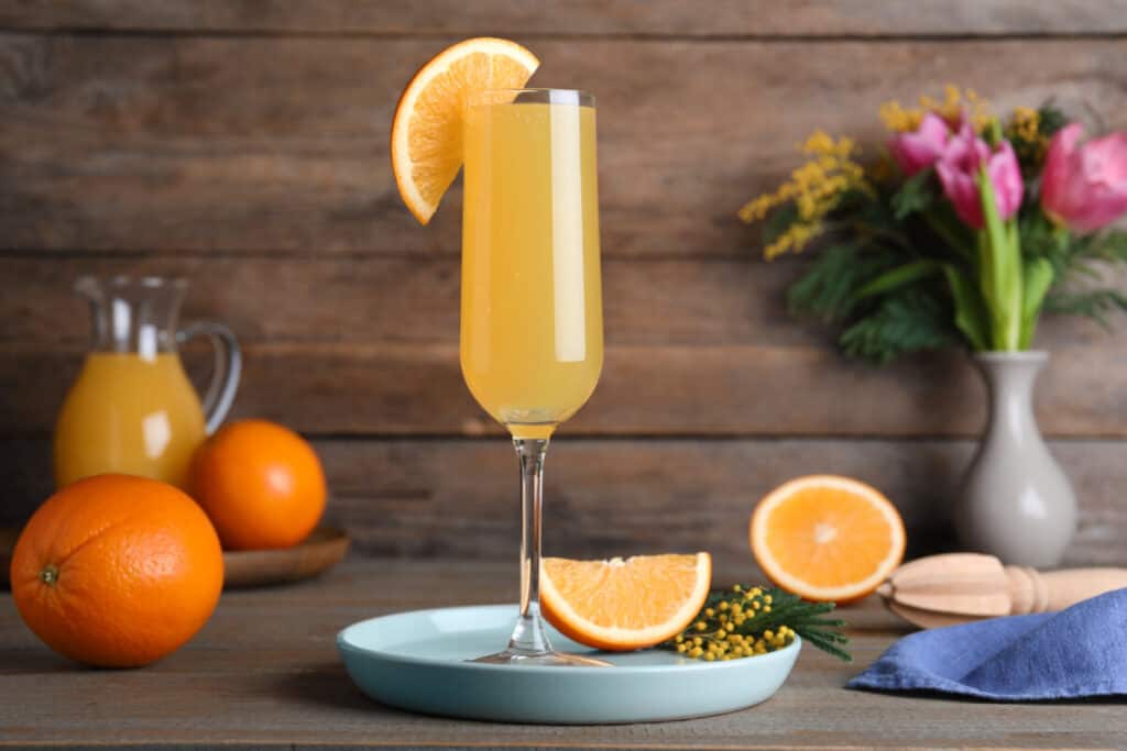 Mimosa in a glass garnished with orange on a wooden table