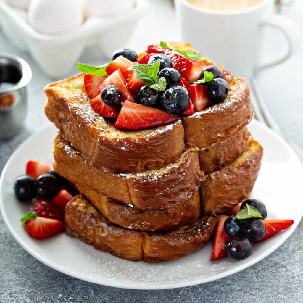 Stack of French toast with strawberries, blueberries, and powdered sugar