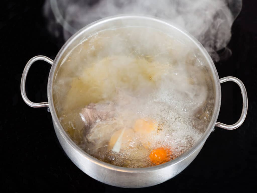 Stock pot full of boiling meat stock with beef and carrots