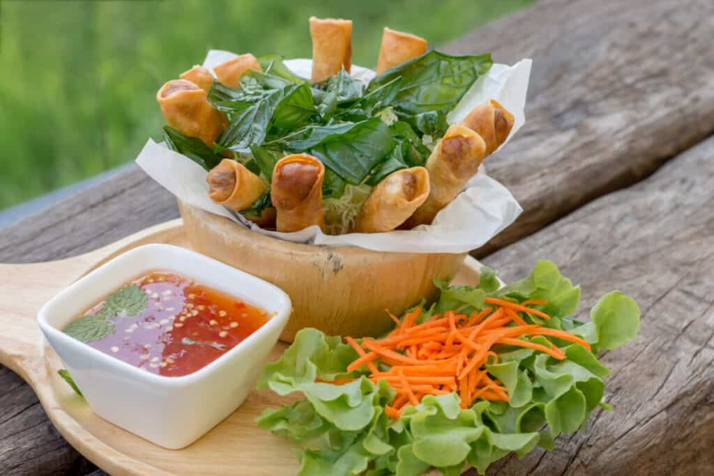 Fried spring rolls with crispy noodle served with sweet and spicy sauce on the wooden plate