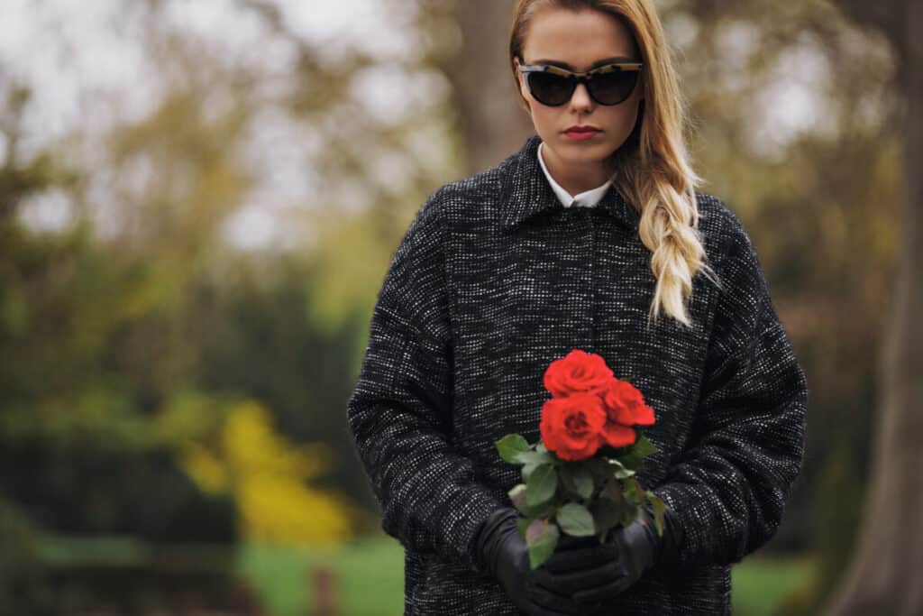 Portrait of a young woman in grey coat at graveyard holding fresh flowers