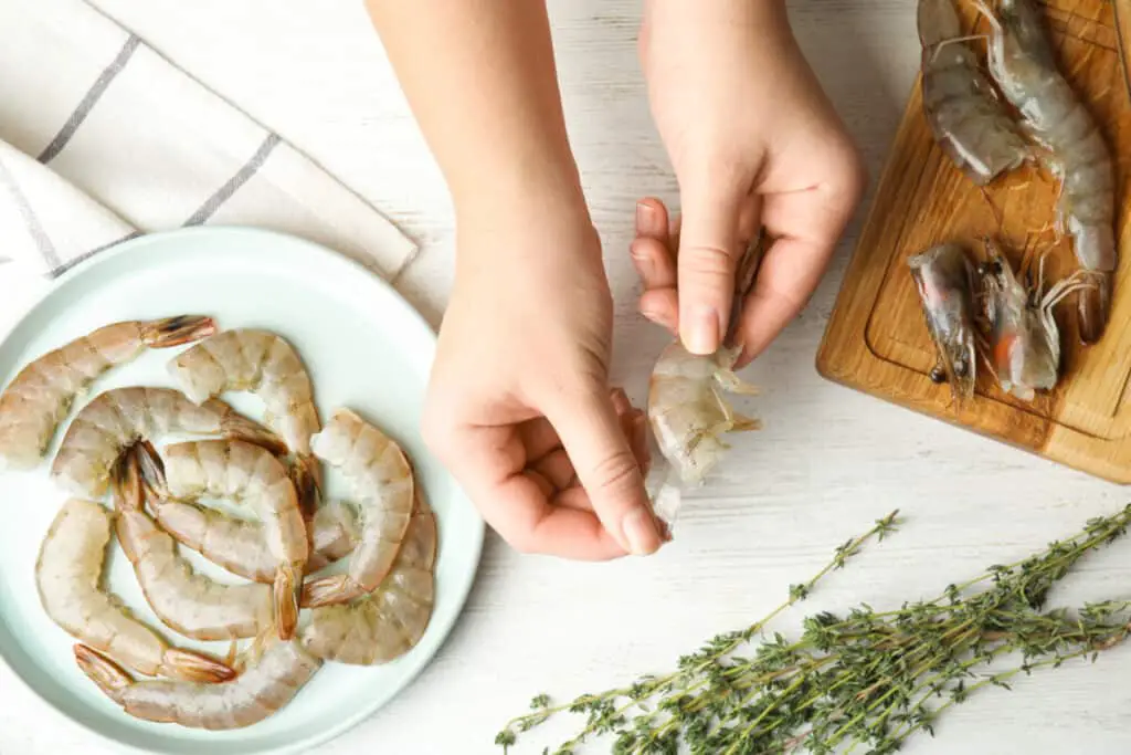 Woman peeling raw shrimp on a white table