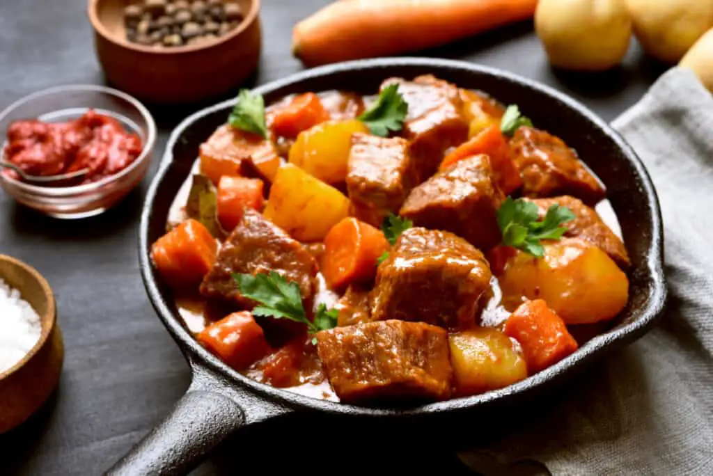Beef meat stewed with potatoes and carrots in cast iron pan