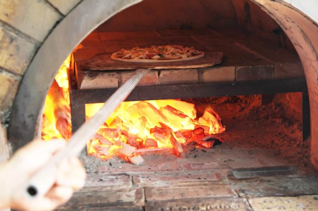 Chef placing fresh pizza in wood fire oven