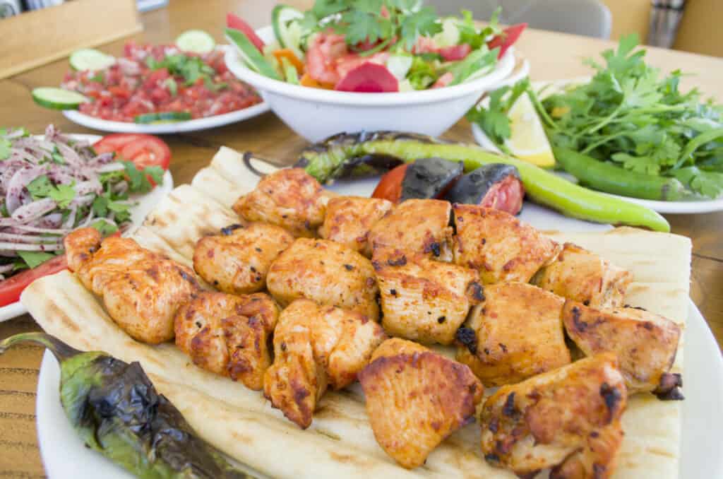 Chicken on skewers with a variety of salads nearby