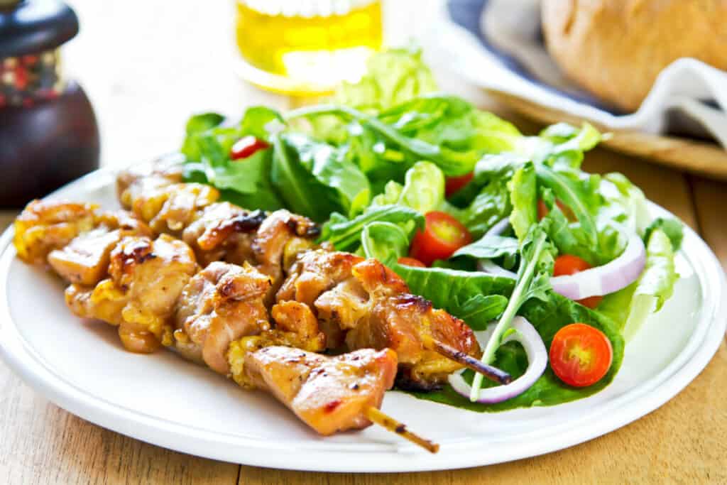 Chicken on skewers with green salad with tomatoes