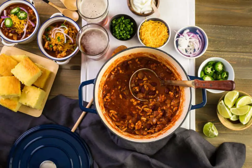 Pot of taco meat with sides of chives, cheese, onions, jalapenos, and lime