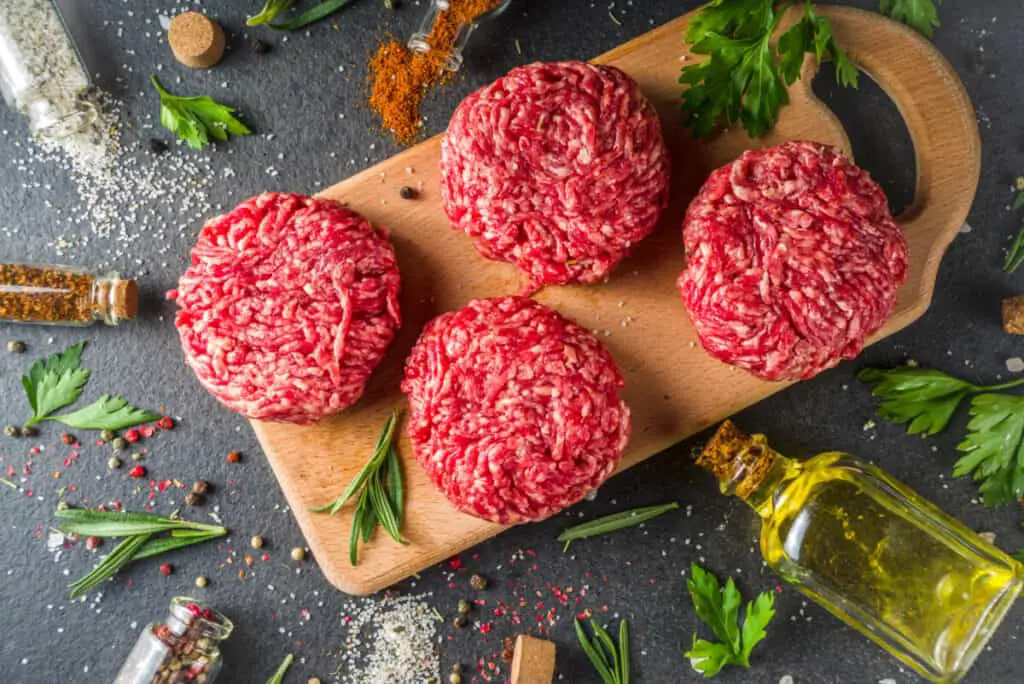 Raw burger patties on a wooden cutting board